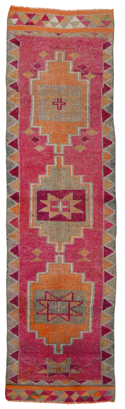 Colorful geometric-patterned rug with pink and orange hues on a white background