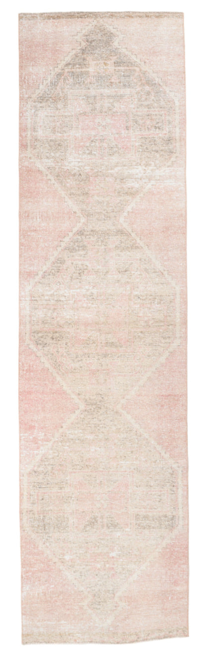 Long narrow rug with a geometric pattern in soft pink and beige tones on a plain background.