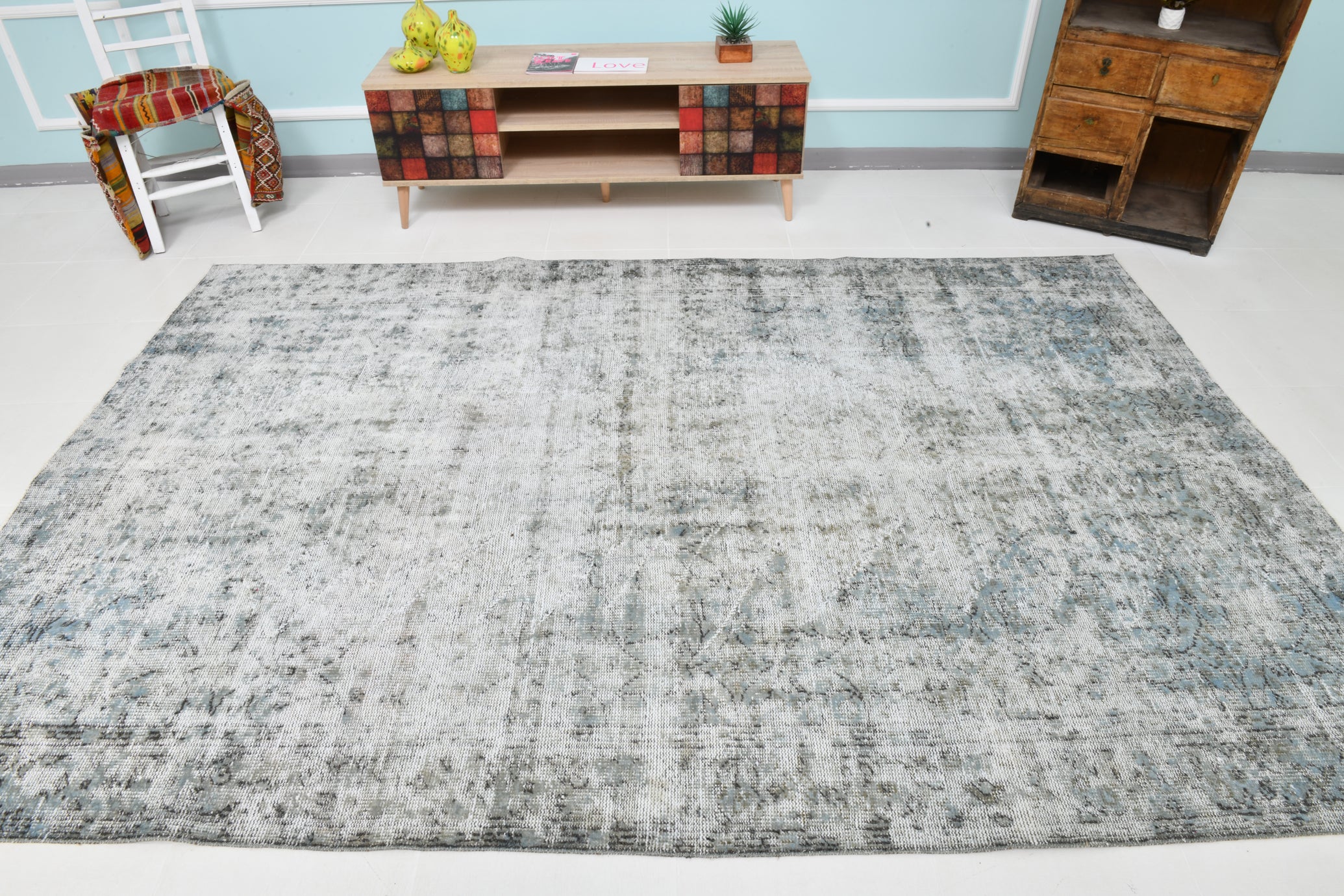 Gray patterned rug on a white floor with a colorful TV stand and wooden bookshelf in the background.