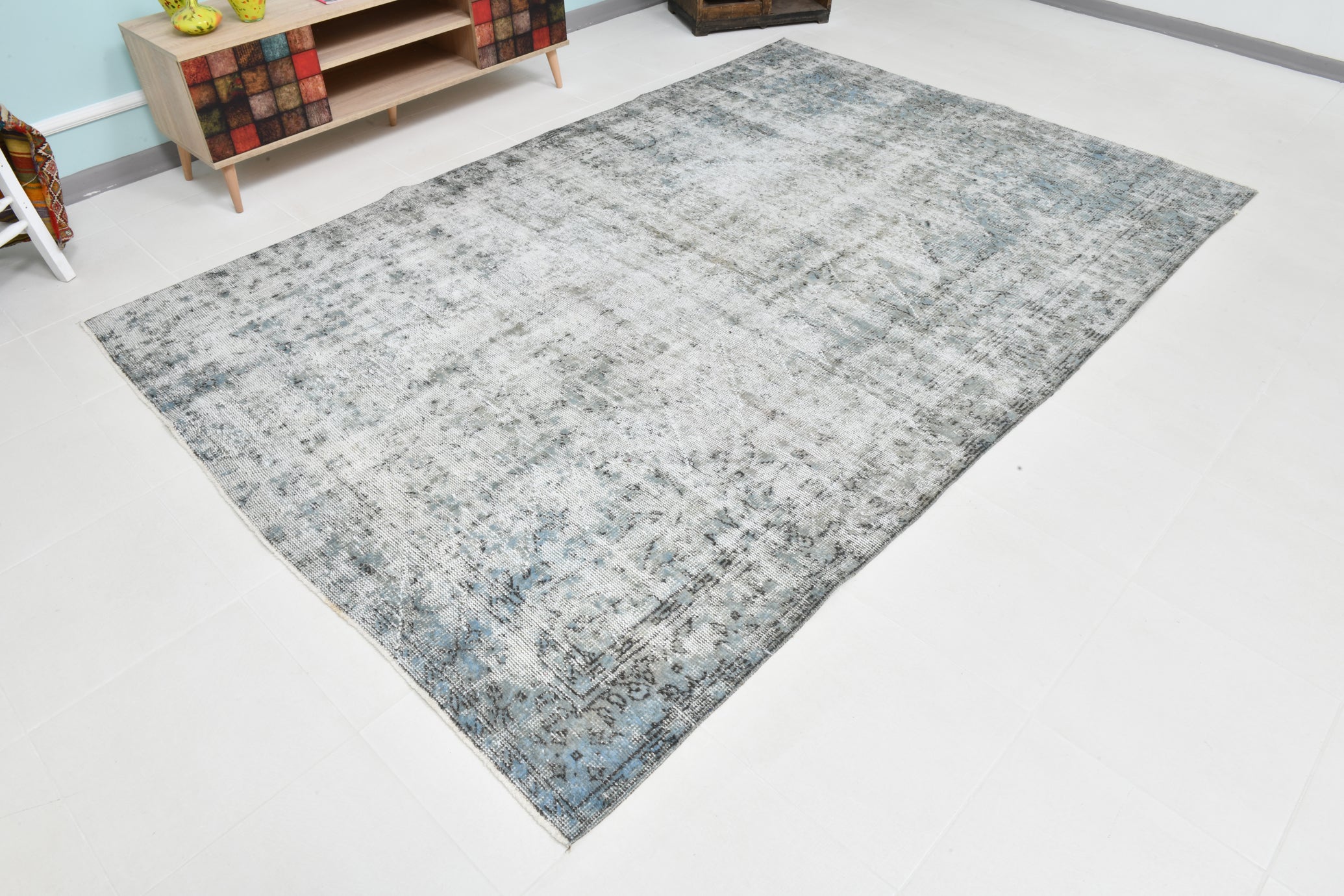 Gray area rug on a white floor with a colorful cabinet in the background.