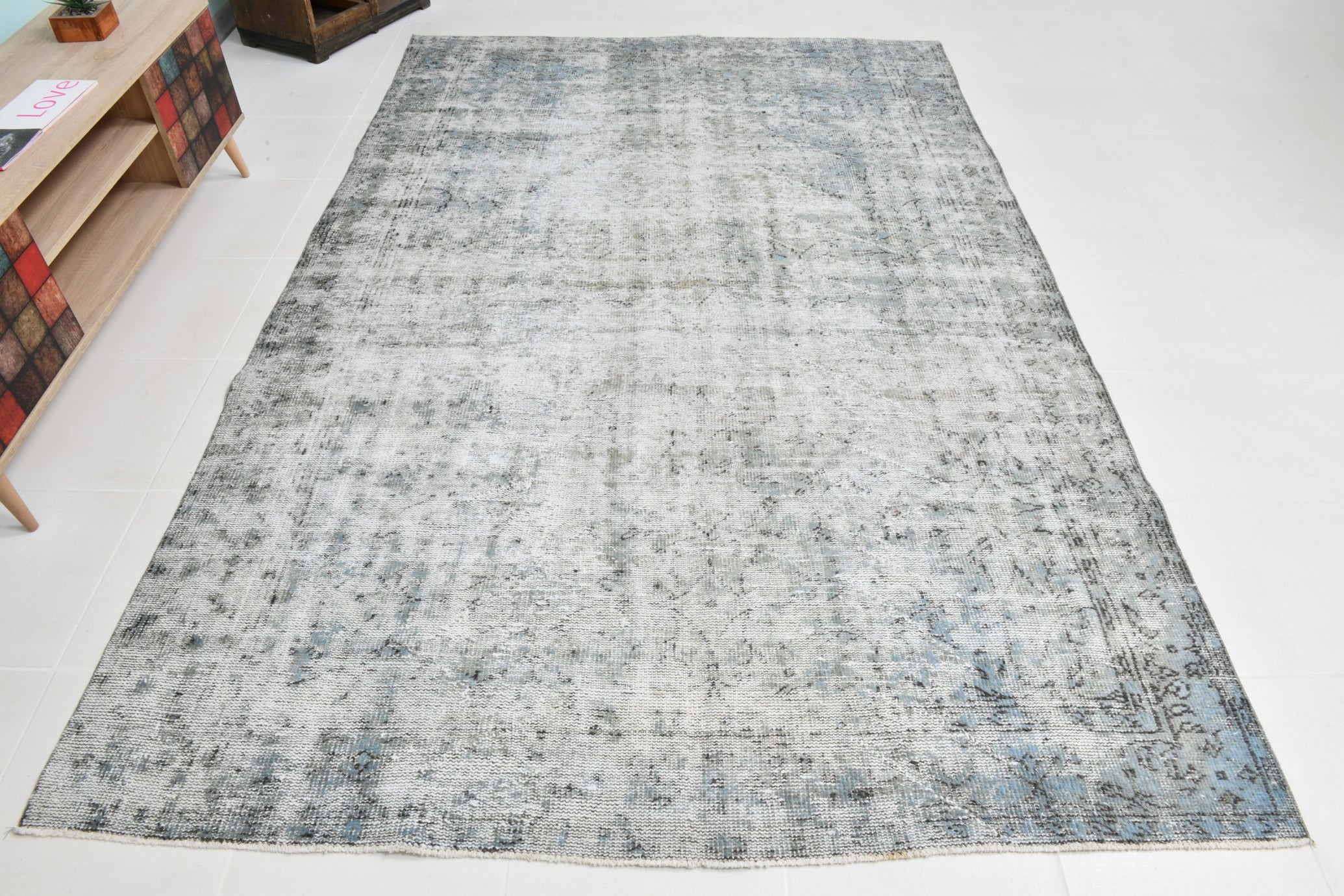 Gray area rug on a white floor with a wooden shelf in the corner.