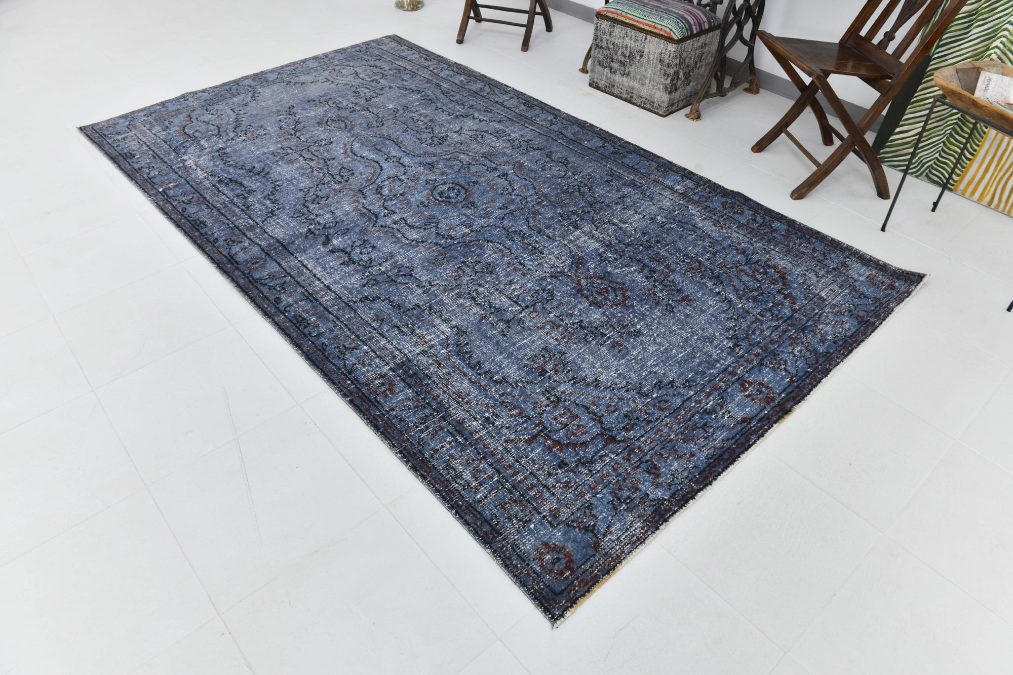 Blue patterned rug on a white floor with chairs and a table in the background