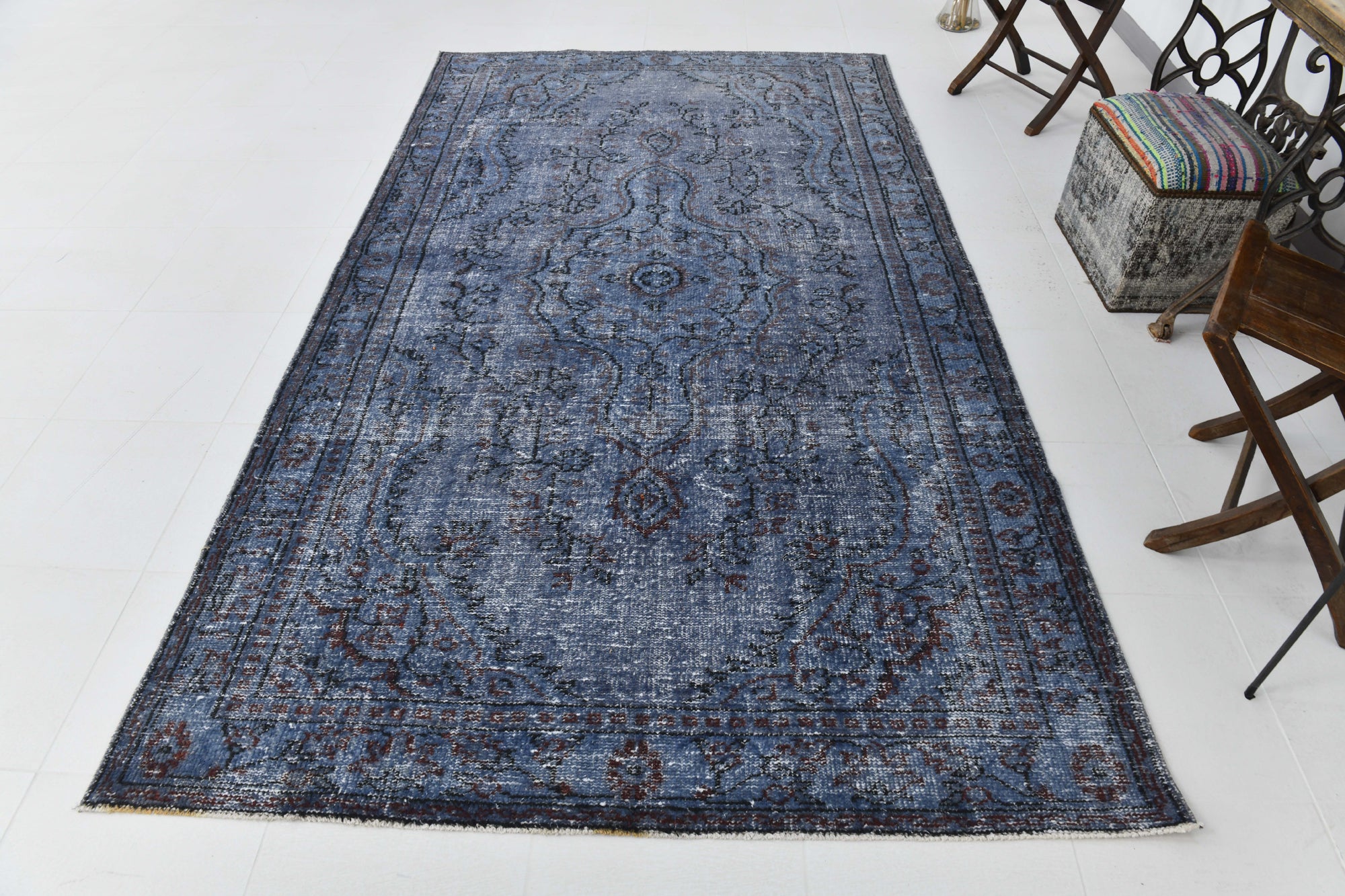 Blue patterned rug on a white floor with chairs and an ottoman in the background.