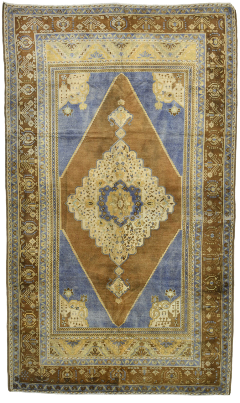 Vintage handwoven rug with a central diamond medallion design, featuring earthy brown, muted blue, and beige tones. The rug showcases intricate geometric borders, floral motifs, and traditional Anatolian-inspired patterns, ideal for bohemian, rustic, or eclectic interior design styles.